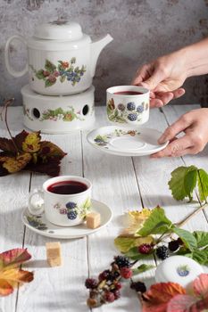 fruit tea with ripe blackberries, vintage still life with beautiful retro set and colander full of berries on the table, summer food, cups with floral-berry pattern, High quality photo