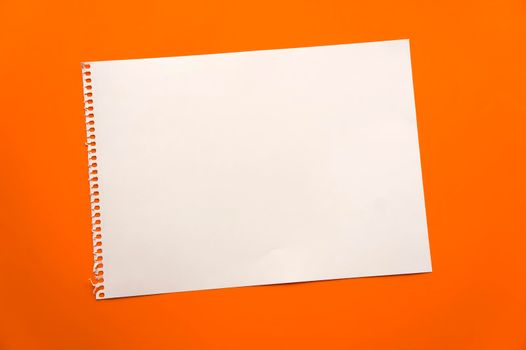 Blank sheet of paper space for design and lettering on a beautiful orange background. A sheet of perforated paper torn from a notepad rests obliquely on the surface. Square sheet of paper copyspace