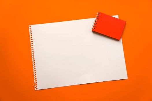 Blank sheet of paper space for design and lettering on a beautiful orange background red notepad sheet. Perforated sheet torn from notepad obliquely lying on the surface. Square sheet of paper copyspace