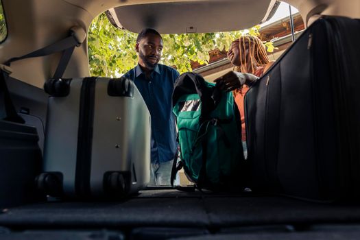 Boyfriend and girlfriend loading baggage in vehicle trunk, leaving on summer holiday together. Couple preparing car with travel bags and luggage to go on vacation trip and drive to destination.