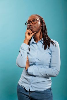 Pensive thoughtful african american woman being meditative and introspective on blue background. Young adult person daydreaming while thinking about problem solution. Studio shot.