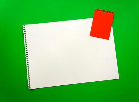 Blank sheet of paper space for design and lettering on a beautiful green background red notepad sheet. Perforated sheet torn from notepad obliquely lying on the surface. Square sheet of paper copyspace