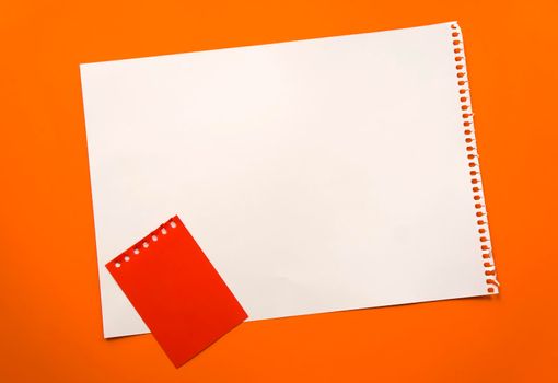 Blank sheet of paper space for design and lettering on a beautiful orange background red notepad sheet. Perforated sheet torn from notepad obliquely lying on the surface. Square sheet of paper copyspace