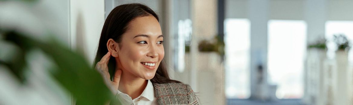 Charming Asian woman with a smile holding mobile phone at the office and looking away