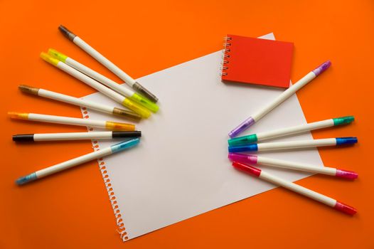 Creative kids, concept. Colorful crayon paints and blank notepad on orange color background, red little notepad. Empty paper for painting, space, template. Education, Back to School concept.