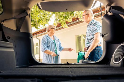 Old couple loading travel bags in trunk to leave on vacation journey with vehicle. People travelling together on retirement holiday trip with trolley and baggage, leisure activity.