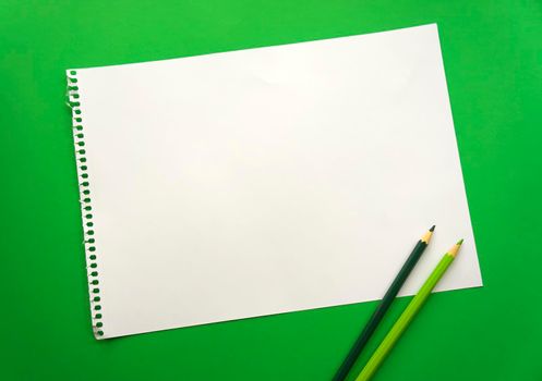 Blank sheet of paper space for design and lettering on a beautiful green background blue pencils. Perforated sheet torn from notepad obliquely lying on the surface. Square sheet of paper. copyspace