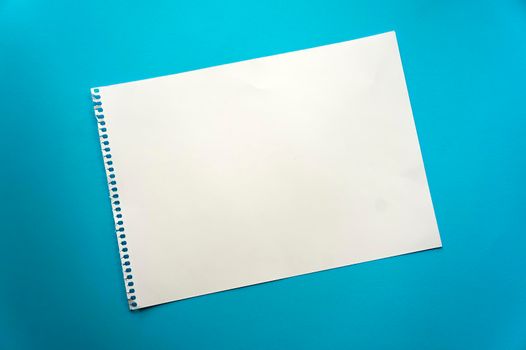 Blank sheet of paper space for design and lettering on a beautiful blue background. A sheet of perforated paper torn from a notepad rests obliquely on the surface. Square sheet of paper copyspace