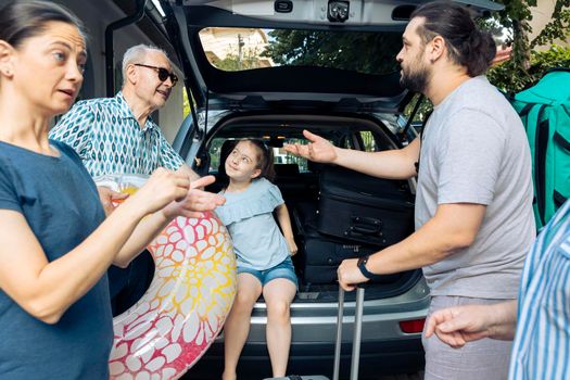European family travelling on vacation trip, loading baggage and inflatable in car trunk to leave at seaside. Little kid, parents and grandparents going on summer holiday with vehicle.