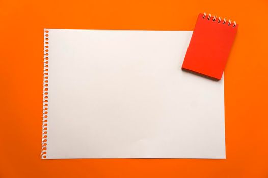 Blank sheet of paper space for design and lettering on a beautiful orange background red notepad sheet. Perforated sheet torn from notepad obliquely lying on the surface. Square sheet of paper copyspace