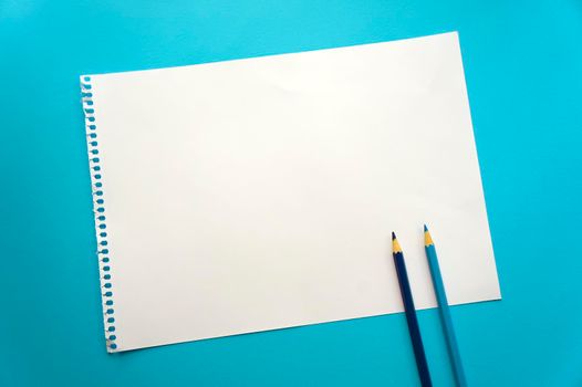 Blank sheet of paper space for design and lettering on a beautiful blue background, blue pencils. A sheet of perforated paper torn from a notepad rests obliquely on the surface. Square sheet copyspace