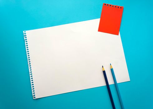 Blank sheet of paper space for design and lettering on a beautiful blue background, blue pencils. A sheet of perforated paper torn from a notepad rests obliquely on the surface. Square sheet copyspace