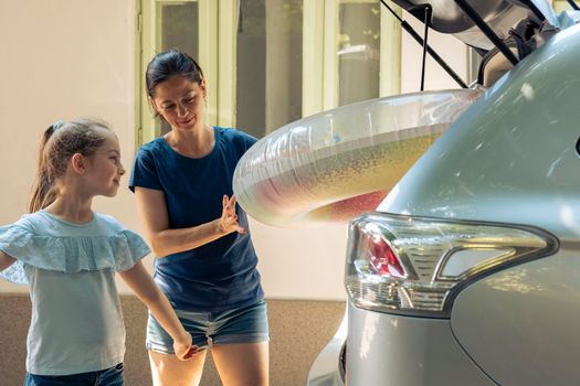 Small family travelling on holiday trip with inflatable and baggage in automobile trunk. Mother with young kid going on summer vacation at seaside. Going on journey adventure with vehicle.