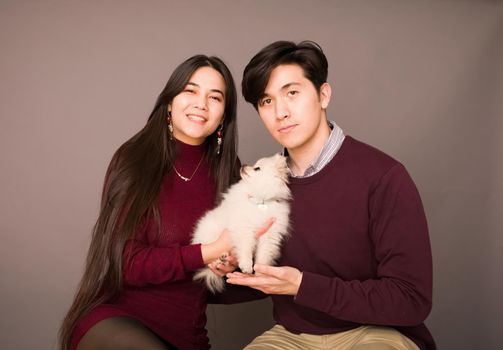 Attractive young biracial couple posing with purebred white Pomeranian puppy