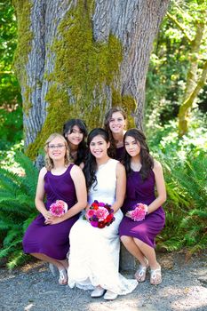 Beautiful biracial young bride smiling with her multiethnic group of four bridesmaids in purple dresses