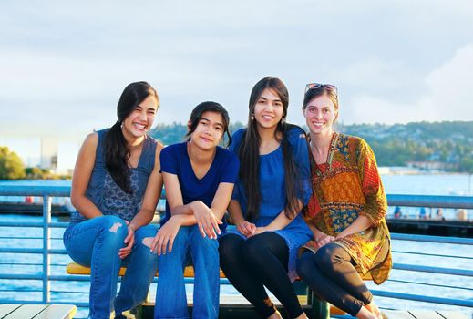 Four young women sitting together, enjoying time at lake, talking.
