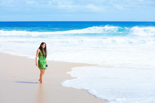 Beautiful teen girl in green dress walking along Hawaiian beach at water's edge