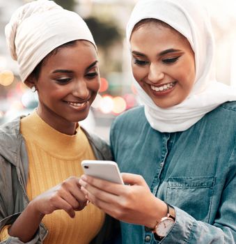 Lets go see this place. two attractive young women wearing headscarves and standing together while using a cellphone in the city
