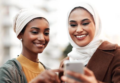 What about this tourist spot here. two attractive young women wearing headscarves and standing together while using a cellphone in the city
