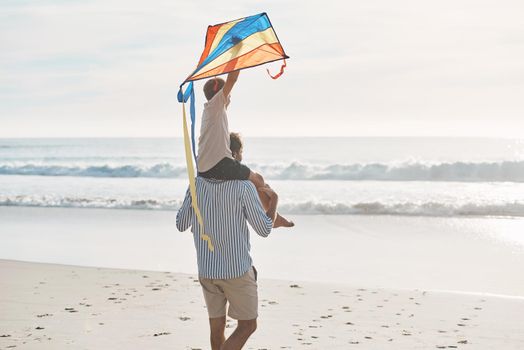 This kite needs to take off. Rearview shot of a young boy being carried on his fathers shoulders and holding a kite on the beach