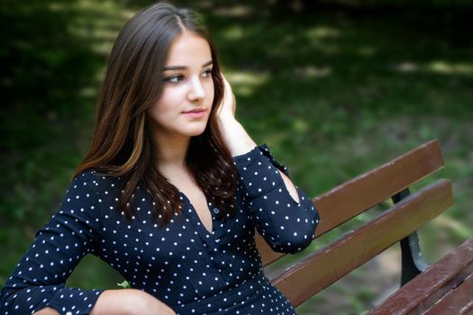 Emotional girl teenager with long hair hairstyle braids in a green shirt sits on a bench in the park. High quality photo