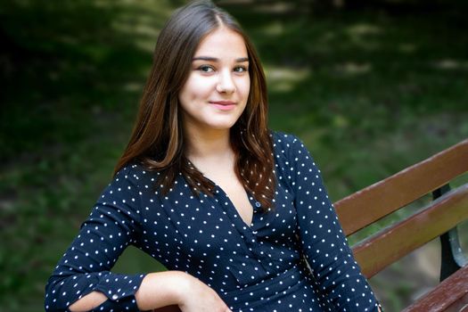 Emotional girl teenager with long hair hairstyle braids in a green shirt sits on a bench in the park. High quality photo