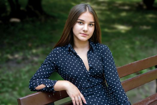 Emotional girl teenager with long hair hairstyle braids in a green shirt sits on a bench in the park. High quality photo