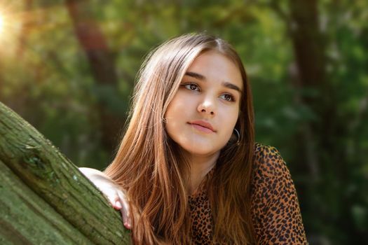 Emotional girl teenager with long hair hairstyle braids in a green shirt sits on a bench in the park. High quality photo