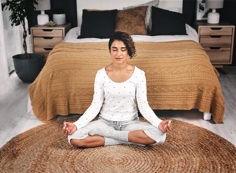 Mental health is just as important as physical health. an attractive young woman sitting and meditating by the foot of her bed in her bedroom