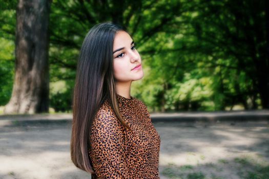 Emotional girl teenager with long hair hairstyle braids in a green shirt sits on a bench in the park. High quality photo