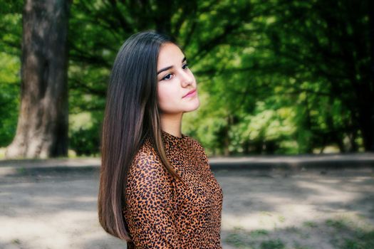 Emotional girl teenager with long hair hairstyle braids in a green shirt sits on a bench in the park. High quality photo