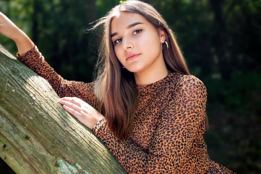 Emotional girl teenager with long hair hairstyle braids in a green shirt sits on a bench in the park. High quality photo