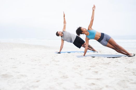 Leading a more active lifestyle together. a young man and woman practising yoga together at the beach