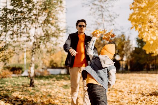 Father and son having fun in autumn park with fallen leaves, throwing up leaf. Child kid boy and his dad outdoors playing with maple leaves