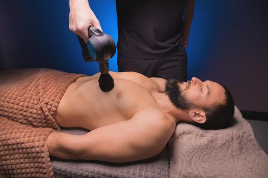 Sports percussion massage in the medical office of the gym. The masseur makes massage exercises. Percussion therapy for regenerating sports body massage. Sports injury rehabilitation concepts