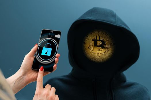 Man without a face in a hood holds a luminous bitcoin icon on a dark background