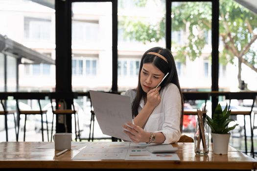 Business asian woman working with paperwork calculator at office while talking on phone