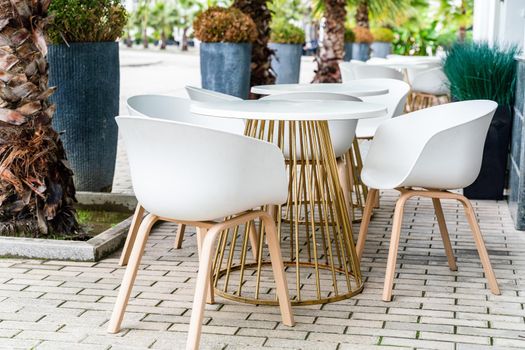 Street cafe with white chairs, green foliage around. Without people, tourism, travel