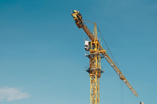 Tower Crane lattice boom hook clear blue sky sun background. Construction site work building installation.