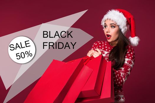 Christmas woman. Beauty model girl in santa hat on red background. Funny laughing surprised woman portrait. Open mouth. True emotions. Red lips and beautiful holiday makeup. Shopping and sale. Shopaholic girl. Black Friday, holiday celebration.