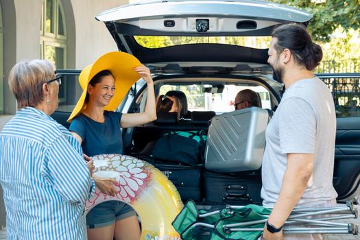 Excited family travelling on seaside holiday, leaving with suitcase and baggage in car trunk. Little girl, parents and grandparents going to sea destination with automobile, to travel on vacation.