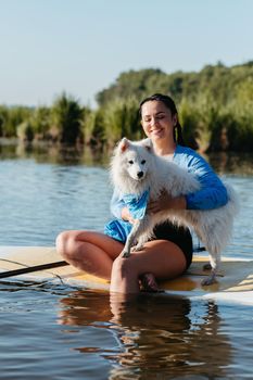 Happy Cheerful Woman Hugging Her Snow-White Dog Japanese Spitz While Sitting on the Sup Board on Lake