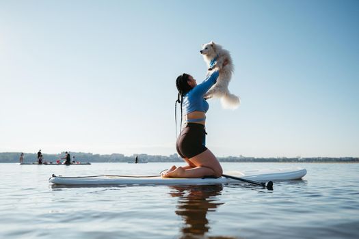 Woman Raising Up Her Dog Japanese Spitz While Sitting on the Sup Board on Lake