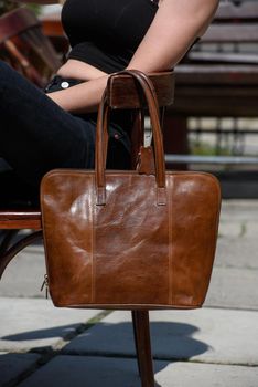 close-up photo of brown leather bag on a wooden chair. outdoors photo