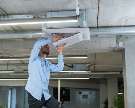 Caucasian bearded man repairing the air conditioner in the office