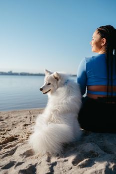 Woman with Locs Sitting on Beach of City Lake with Her Best Friend, Snow-White Dog Breed Japanese Spitz