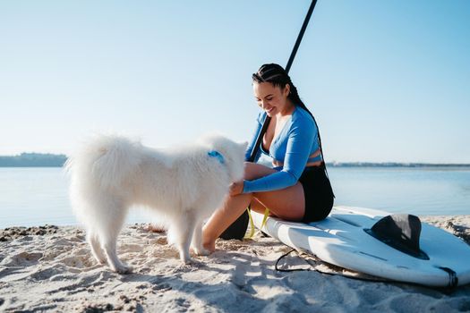 Cheerful Woman with Dreads Preparing to Paddleboarding with Her Snow-White Dog Breed Japanese Spitz, Early Morning on City Lake