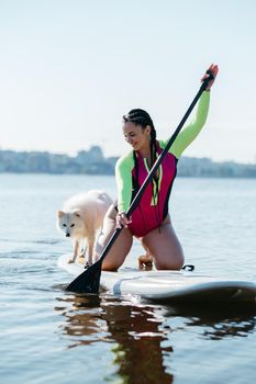 Happy Cheerful Woman Paddleboarding on the City Lake at Early Morning with Her Dog Japanese Spitz Sitting on Sup Board