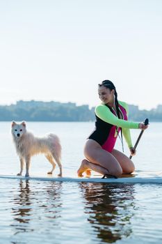 Happy Cheerful Woman Paddleboarding on the City Lake at Early Morning with Her Dog Japanese Spitz Sitting on Sup Board