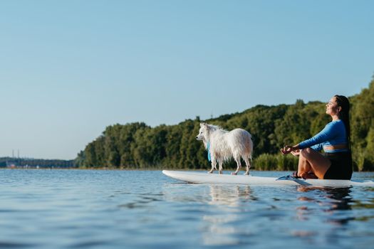 Young Woman Meditating on the City Lake While Sitting on Sup Board with Her Dog Japanese Spitz